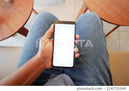 Individual comfortably holding a smartphone in a casual and relaxed setting during the daytime, Individual comfortably holding a smartphone in a casual and relaxed setting during the daytime, 124729349