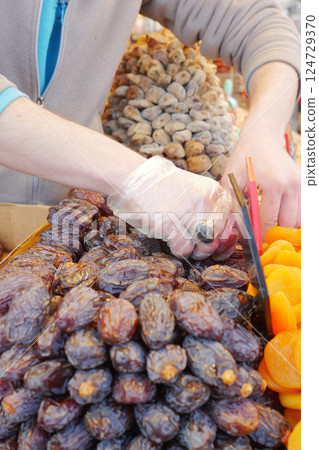 Carefully Choosing a Variety of Dried Fruits at a Vendors Market Stall for Cooking Carefully Choosing a Variety of Dried Fruits at a Vendors Market Stall for Cooking 124729370