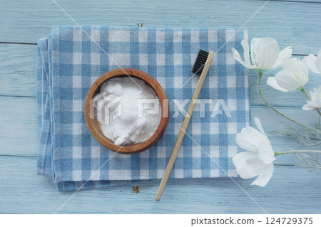 A wooden bowl of baking soda, a bamboo toothbrush, and a glass jar on a fabric A wooden bowl of baking soda, a bamboo toothbrush, and a glass jar on a fabric 124729375