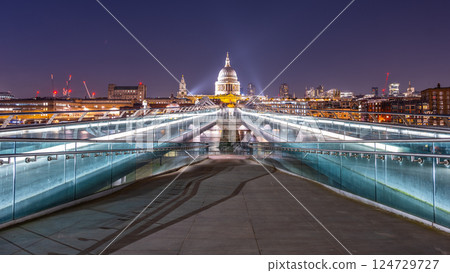 Visitors enjoy an evening walk across the Millennium Bridge, with St. Paul's Cathedral illuminated in the background. The River Thames reflects the city lights, creating a vibrant atmosphere. Visitors enjoy an evening walk across the Millennium Bridge, with St. Paul's Cathedral illuminated in the background. The River Thames reflects the city lights, creating a vibrant atmosphere. 124729727