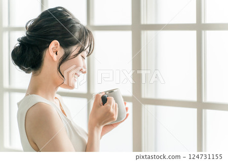 一個放鬆的亞洲女人，早上在家裡用保溫杯喝茶和熱水 (Onkatsu) 124731155