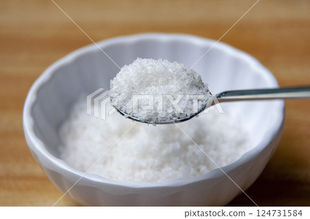 Close up of a spoon filled with coarse salt, held above a white bowl containing more salt Close up of a spoon filled with coarse salt, held above a white bowl containing more salt 124731584