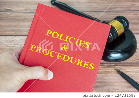 Hand holding Policies and Procedures book with gavel on a wooden table background 124731592