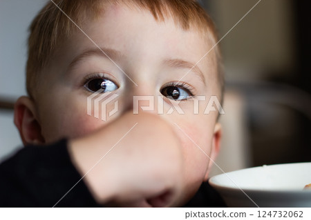 Two-year-old child with brown eyes is eating at a high table, baby's head Two-year-old child with brown eyes is eating at a high table, baby's head 124732062