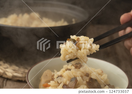 他用筷子夾起一碗用陶鍋煮的蛤蜊飯。 他用筷子夾起一碗用陶鍋煮的蛤蜊飯。 124733037