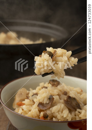 Using chopsticks, he picks up a bowl of clam rice cooked in a clay pot. Using chopsticks, he picks up a bowl of clam rice cooked in a clay pot. 124733039
