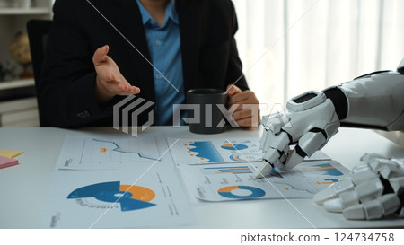 Business Meeting with Human and Robot Collaboration Analyzing Data Charts for Project Planning and Decision Making in Modern Office Environment. Noogenesis 124734758