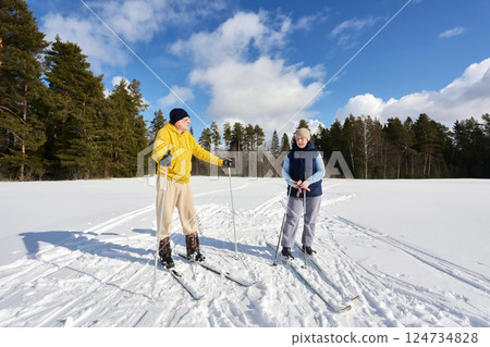 Skiing through snowy field on edge of forest, white couple in their 50s took break to rest. Skiing through snowy field on edge of forest, white couple in their 50s took break to rest. 124734828