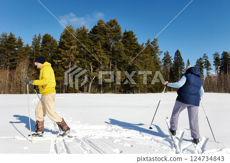 Mature couple in 50s enjoys cross country skiing, gliding across vast snow covered field and navigating through winter landscape with steady resolve. Mature couple in 50s enjoys cross country skiing, gliding across vast snow covered field and navigating through winter landscape with steady resolve. 124734843