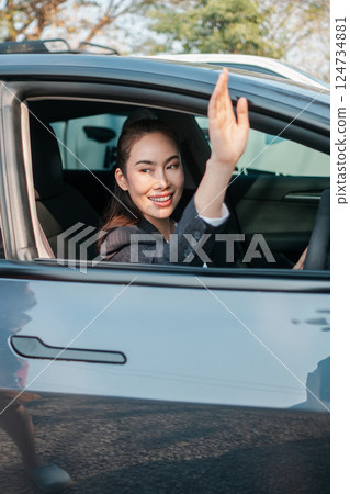 Smiling businesswoman in a car, waving through the window, showcasing a positive and professional demeanor. Smiling businesswoman in a car, waving through the window, showcasing a positive and professional demeanor. 124734881