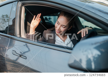 Confident businesswoman in a car, smiling and showing an OK gesture, symbolizing success and positivity in a modern urban environment. 124734883