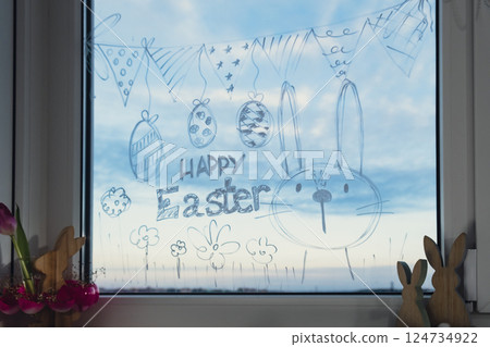 HAPPY EASTER text on creative painted window with white marker. Easter bunny rabbit decoration on big clear window. Springtime idea home decoration 124734922