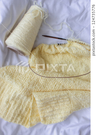 Yellow cotton knitting with knitting needles on white sheet. Soft yellow knitwear with circle needles. Knitting pattern background. Knitting lifestyle. Cozy hobby. Warm knitwear. Craft product concept Yellow cotton knitting with knitting needles on white sheet. Soft yellow knitwear with circle needles. Knitting pattern background. Knitting lifestyle. Cozy hobby. Warm knitwear. Craft product concept 124735776
