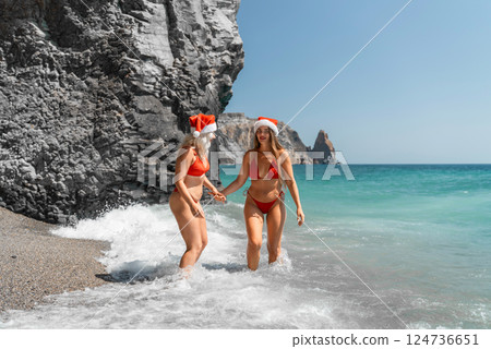Women in Santa Claus hats run into the sea dressed in red swimsuits. Celebrating the New Year in a hot country 124736651