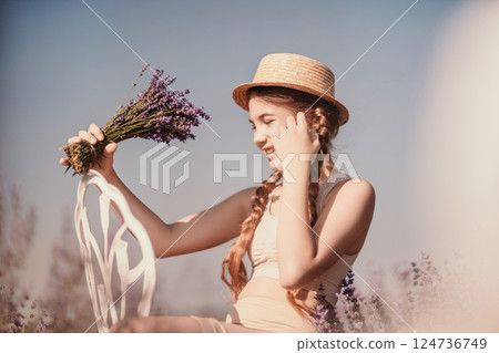 girl sitting field lavender and wearing a straw hat. She is smiling and holding a bouquet of flowers girl sitting field lavender and wearing a straw hat. She is smiling and holding a bouquet of flowers 124736749
