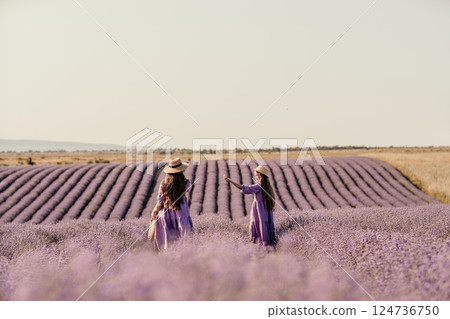 Mom and daughter are running through a lavender field dressed in purple dresses, long hair flowing and wearing hats. The field is full of purple flowers and the sky is clear. Mom and daughter are running through a lavender field dressed in purple dresses, long hair flowing and wearing hats. The field is full of purple flowers and the sky is clear. 124736750