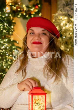 Woman Christmas Lantern Festive - A woman in a red beret and white sweater smiles while holding a red lantern in front of a Christmas tree. 124736751