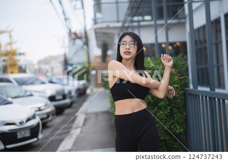 Young woman stretching outdoors in urban setting, wearing black sports outfit, showcasing fitness and wellness lifestyle during daytime exercise routine. Young woman stretching outdoors in urban setting, wearing black sports outfit, showcasing fitness and wellness lifestyle during daytime exercise routine. 124737243