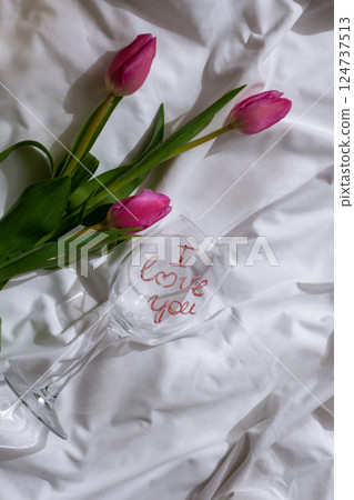 Wine glass with words I LOVE YOU Fresh bouquet of pink tulip flowers on bed. Gift present idea for holiday birthday 8 March Mother's Day Valentine's day Women's Day 124737513