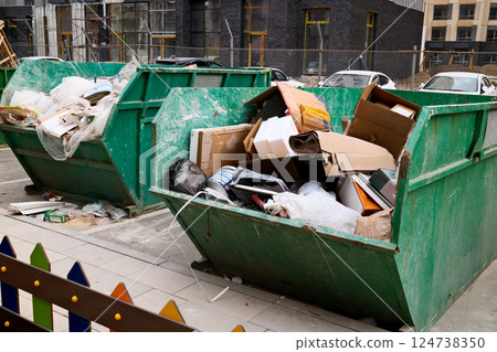 Overflowing green construction dumpster filled with cardboard boxes and building waste at urban construction site 124738350