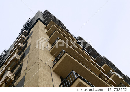 Modern residential high-rise building with balconies and air conditioning units, low angle view against clear sky Modern residential high-rise building with balconies and air conditioning units, low angle view against clear sky 124738352