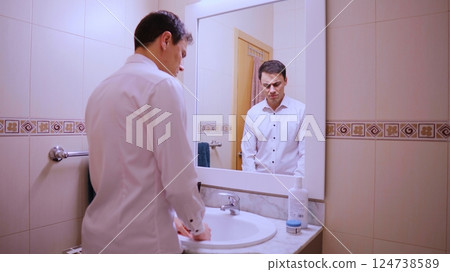 Depressed businessman looking at his sad reflection in bathroom mirror Depressed businessman looking at his sad reflection in bathroom mirror 124738589