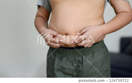 A fat child with a fat belly holds his stomach with his hands. A fat child with a fat belly holds his stomach with his hands. 124739722