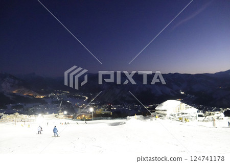 The slopes reflecting the white light of the night lights and the mountain ridges faintly visible against the deep blue sky 124741178