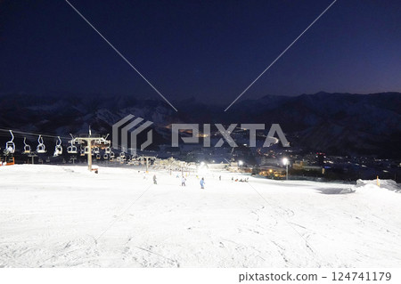 The slopes reflecting the white light of the night lights and the mountain ridges faintly visible against the deep blue sky 124741179
