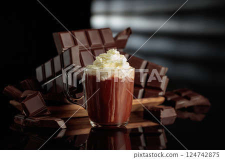 A mug of hot chocolate with whipped cream against broken bitter chocolate bars. A mug of hot chocolate with whipped cream against broken bitter chocolate bars. 124742875