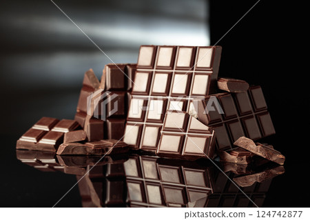 Broken bitter chocolate bars on a black glossy background. Broken bitter chocolate bars on a black glossy background. 124742877
