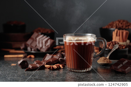 Glass mug of hot chocolate with ingredients on a black kitchen table. 124742905