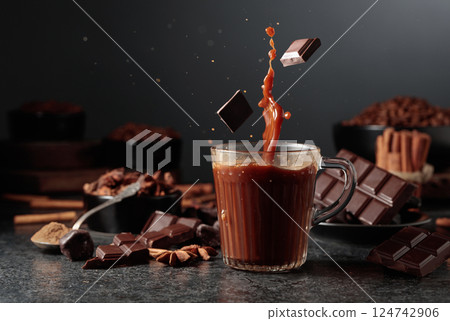 Pieces of dark chocolate fall into a mug of cocoa drink. 124742906