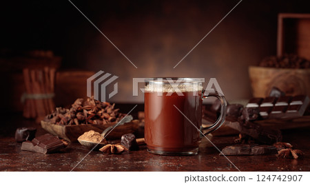 Glass mug of hot chocolate with ingredients on a brown background. 124742907