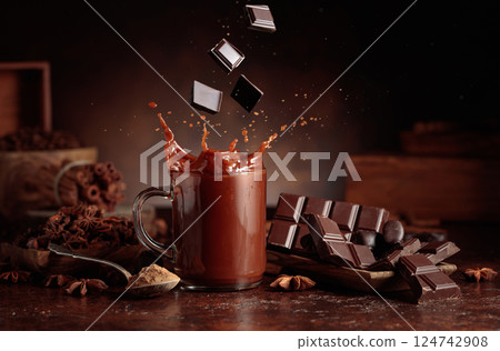 Pieces of dark chocolate fall into a glass of cocoa drink. 124742908