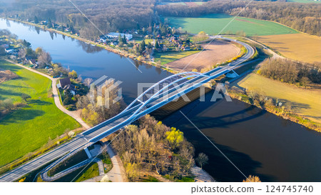 The modern Bohumil Hrabal's Bridge connects two scenic banks over the Labe River in Litol, Lysa nad Labem. Lush green landscapes surround the bridge, showcasing nature's beauty. 124745740