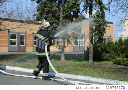Fireman in protective costume watering plant territory with syringe. Rescue team training of firefighting. Fireman in protective costume watering plant territory with syringe. Rescue team training of firefighting. 124746678