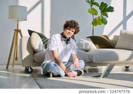 Portrait handsome young male looking at camera sitting on floor near with laptop at home 124747576