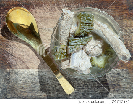 Top view of Boiled bitter gourd soup (Boiled bitter melon soup) with Pork spare rib in Glass bowl served with Brass spoon. Top view of Boiled bitter gourd soup (Boiled bitter melon soup) with Pork spare rib in Glass bowl served with Brass spoon. 124747585