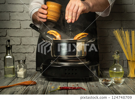 A chef seasons chicken feet with salt in a pot on the stove, creating a flavorful dish. Fresh ingredients are arranged around the pot, enhancing the process of making broth in a modern kitchen setting 124748709