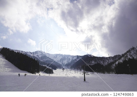 The blue sky is visible through gaps in the thick clouds, and the sun is shining down on the slopes of the ski slopes. 124749863