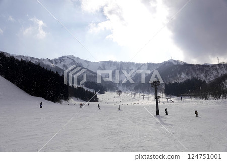 The blue sky is visible through gaps in the thick clouds, and the sun is shining down on the slopes of the ski slopes. 124751001