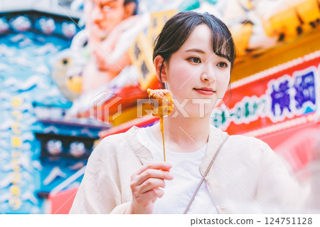 A young woman eating the famous kushikatsu in Shinsekai, Osaka 124751128