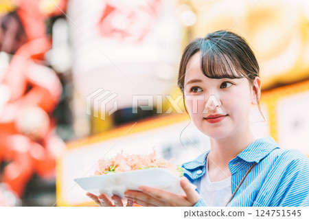 A woman eating the famous takoyaki in Dotonbori, Osaka A woman eating the famous takoyaki in Dotonbori, Osaka 124751545