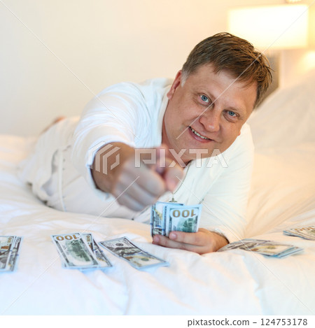 Rich man with pile of cash in bed points at camera 124753178