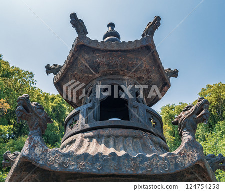 Ancient lantern stands tall amidst lush greenery in a serene outdoor setting under a clear blue sky 124754258
