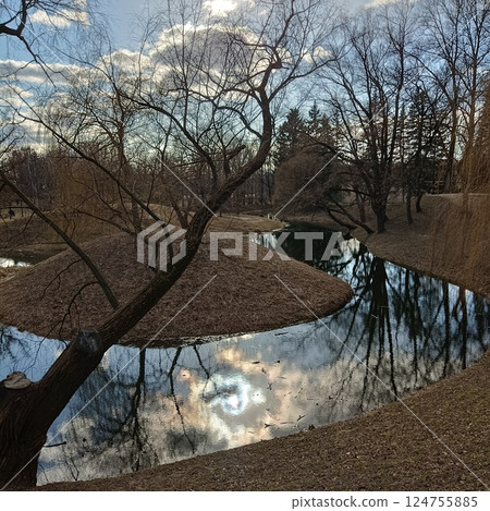 Tranquil river winding through a serene landscape, bare trees reflecting in calm waters under a cloudy sky. Peaceful and serene natural scenery 124755885