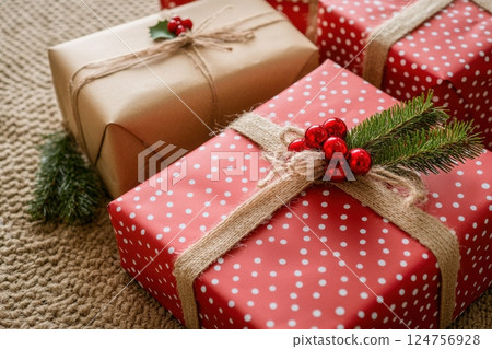 festive Christmas gifts wrapped in red and natural kraft paper, adorned with silk ribbons and twine bows, featuring polka dots, snowflakes, and classic holiday patterns, cozy holiday still life 124756928