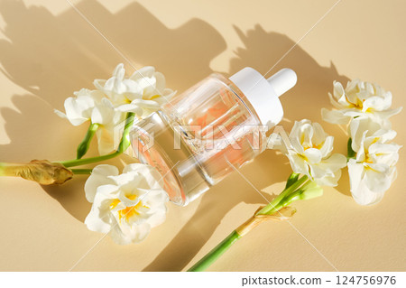 A bottle of luxury serum with petals on a beige background with daffodils. A bottle of luxury serum with petals on a beige background with daffodils. 124756976