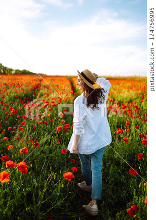 Young girl in hat posing in the poppy field. Portrait of curly girl walking in poppy field at sunset. Summertime. Young girl in hat posing in the poppy field. Portrait of curly girl walking in poppy field at sunset. Summertime. 124756995